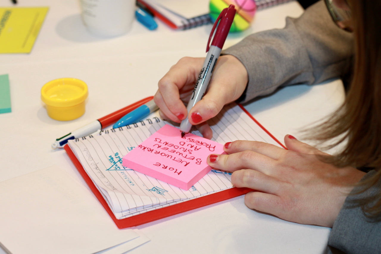 Person writing on a pink post-it note